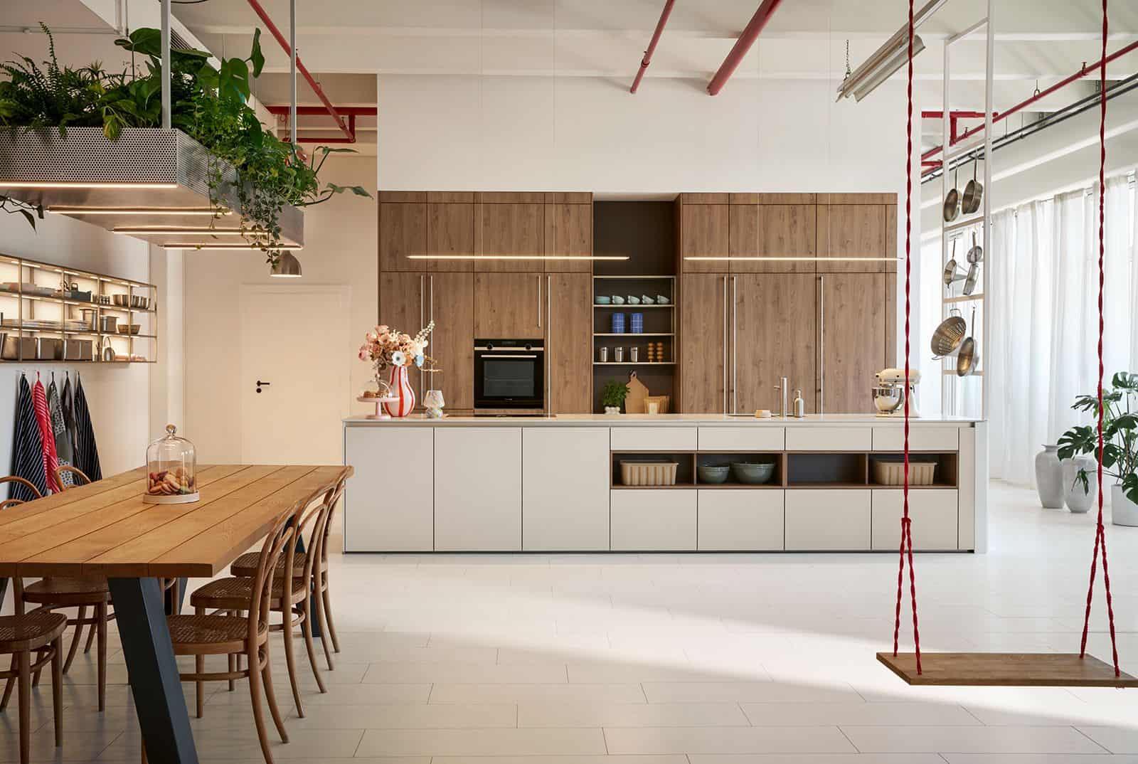 Offene Loft-Küche mit Holzfronten, heller Kücheninsel, langem Esstisch und Schaukel an der Decke