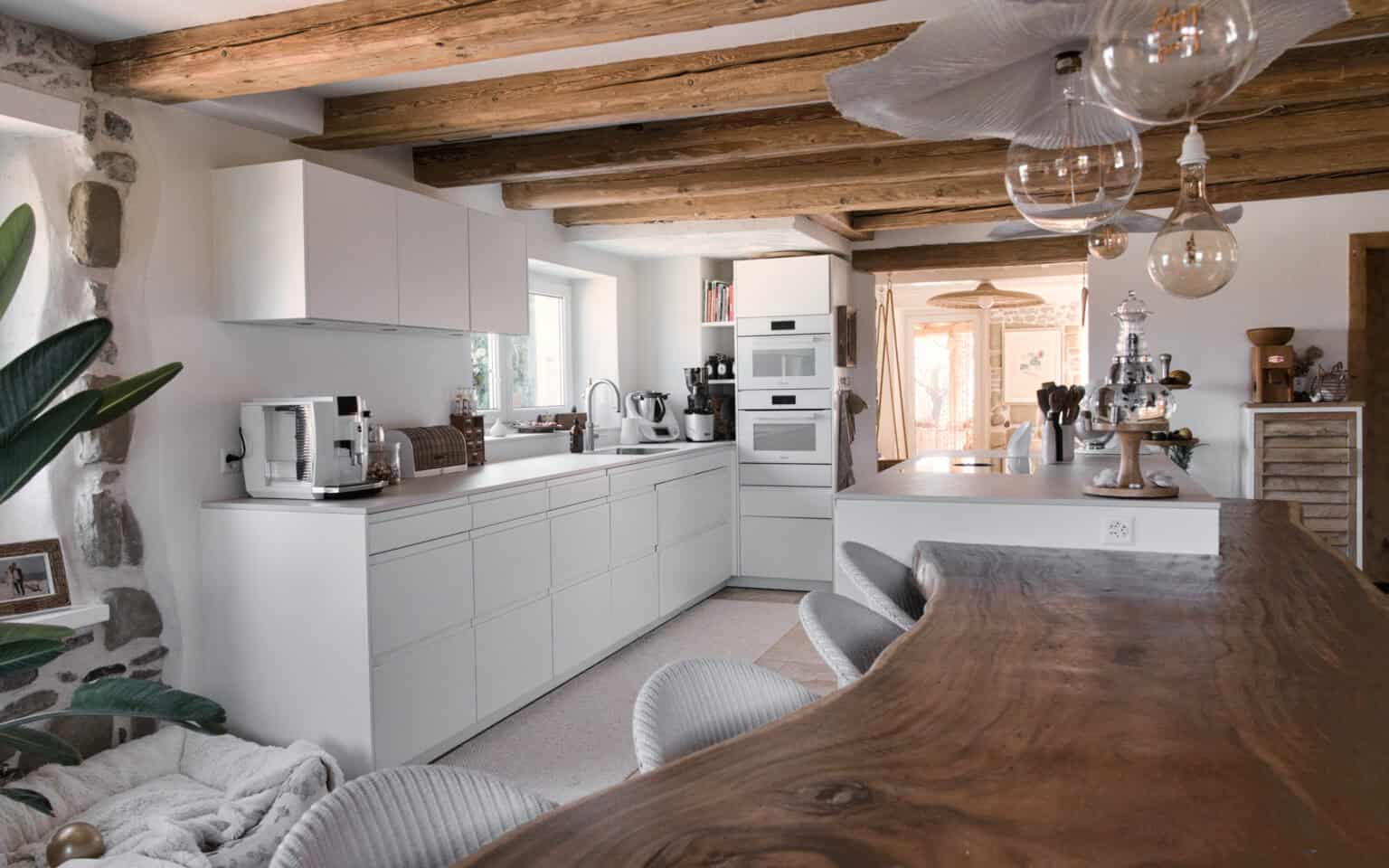 Weisse Küche mit Theke aus massivem Holz unter Holzbalken