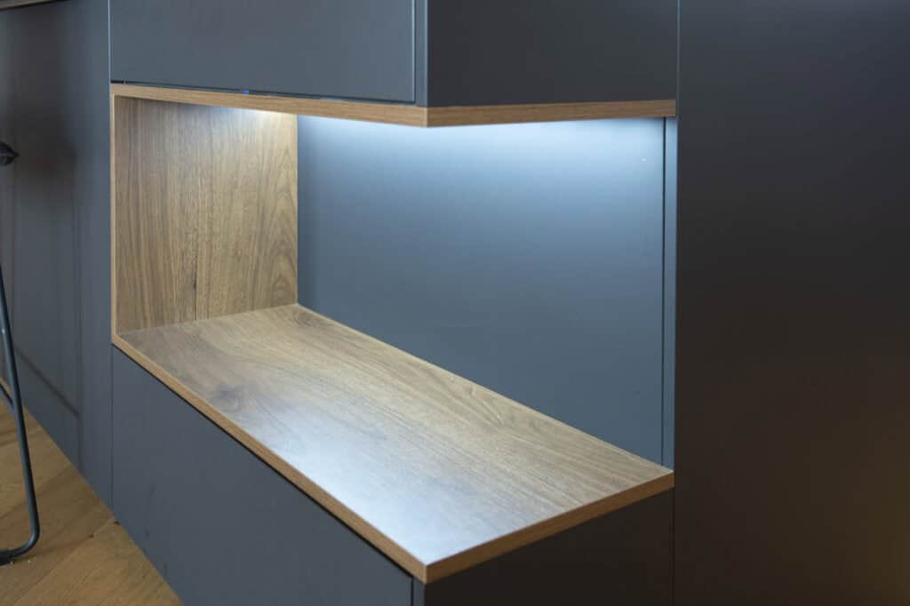 Moderne blaue Küchenzeile mit Holzablage und Beleuchtung.
