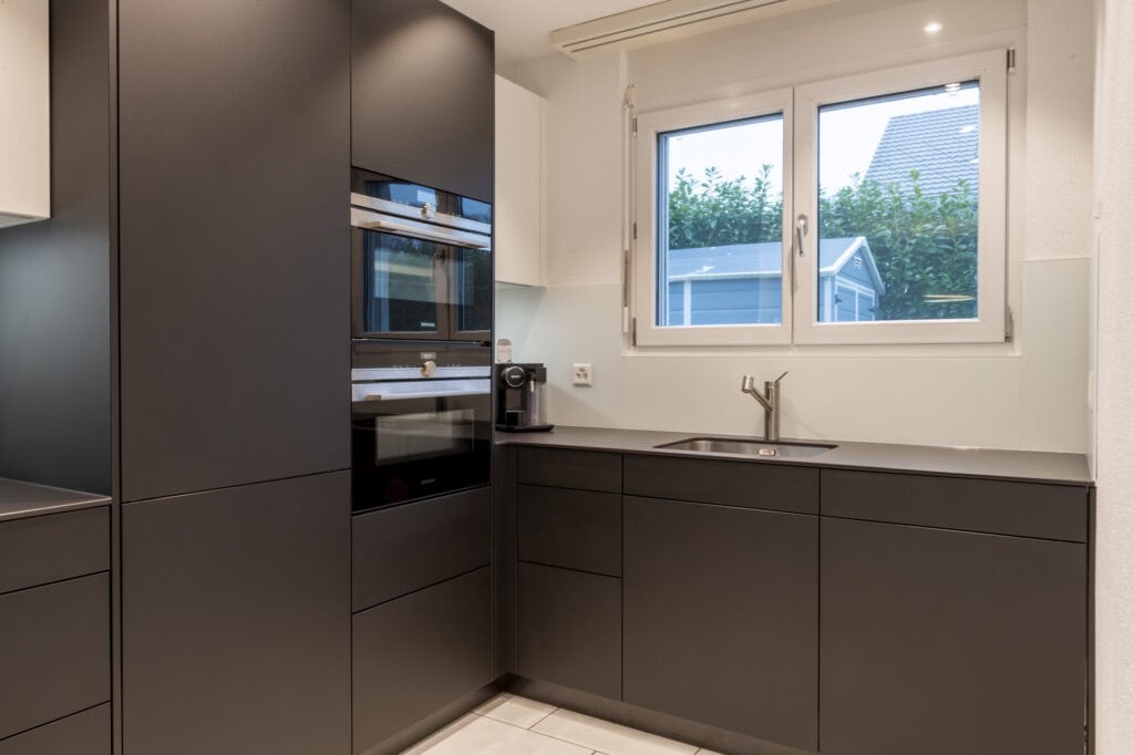 Dunkle moderne Küche mit Fenster und Blick ins Freie, minimalistische Gestaltung.