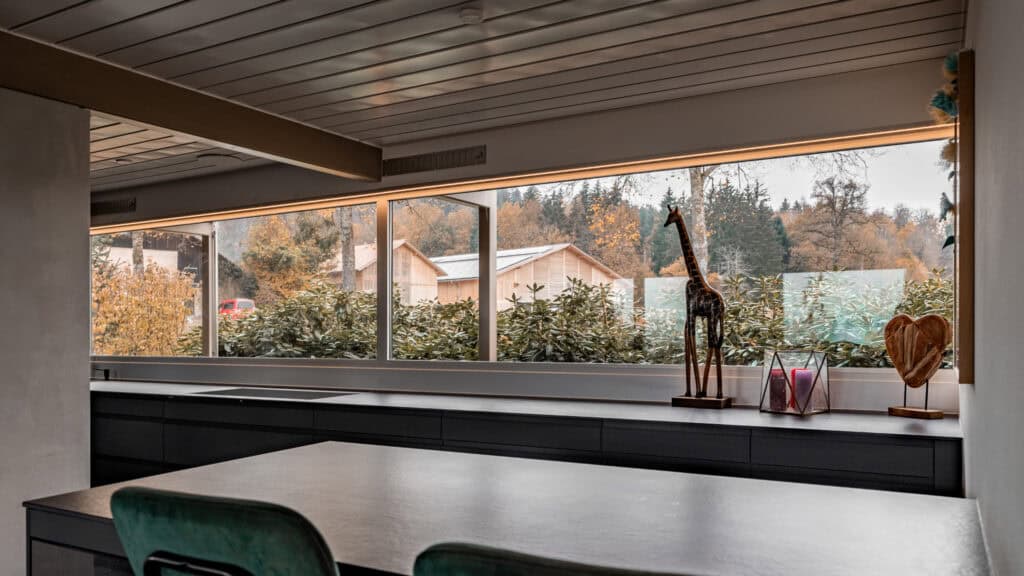 Große Fensterfront in der modernen Küche mit Blick ins Grüne und natürliche Lichtverhältnisse.