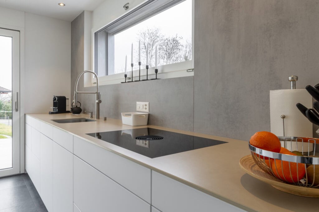 Moderne Küche mit weißen Schränken, grauem Wand und großem Fenster für helle Kochbereiche.