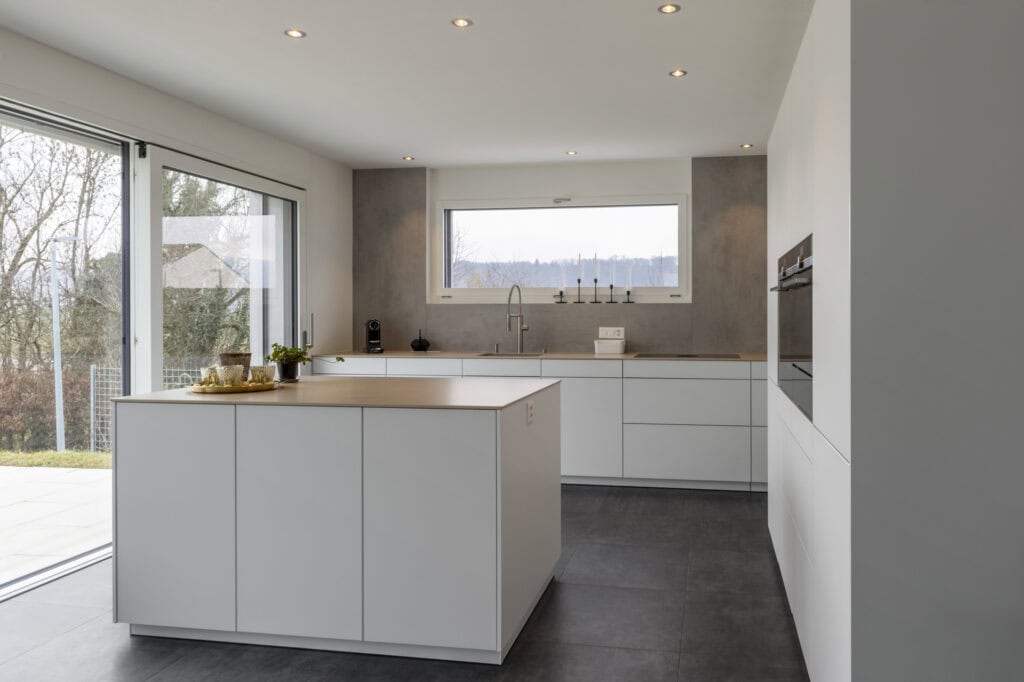 Weiße Küche mit Insel, viel Tageslicht und moderner Ausstattung für stilvolles Kochen.