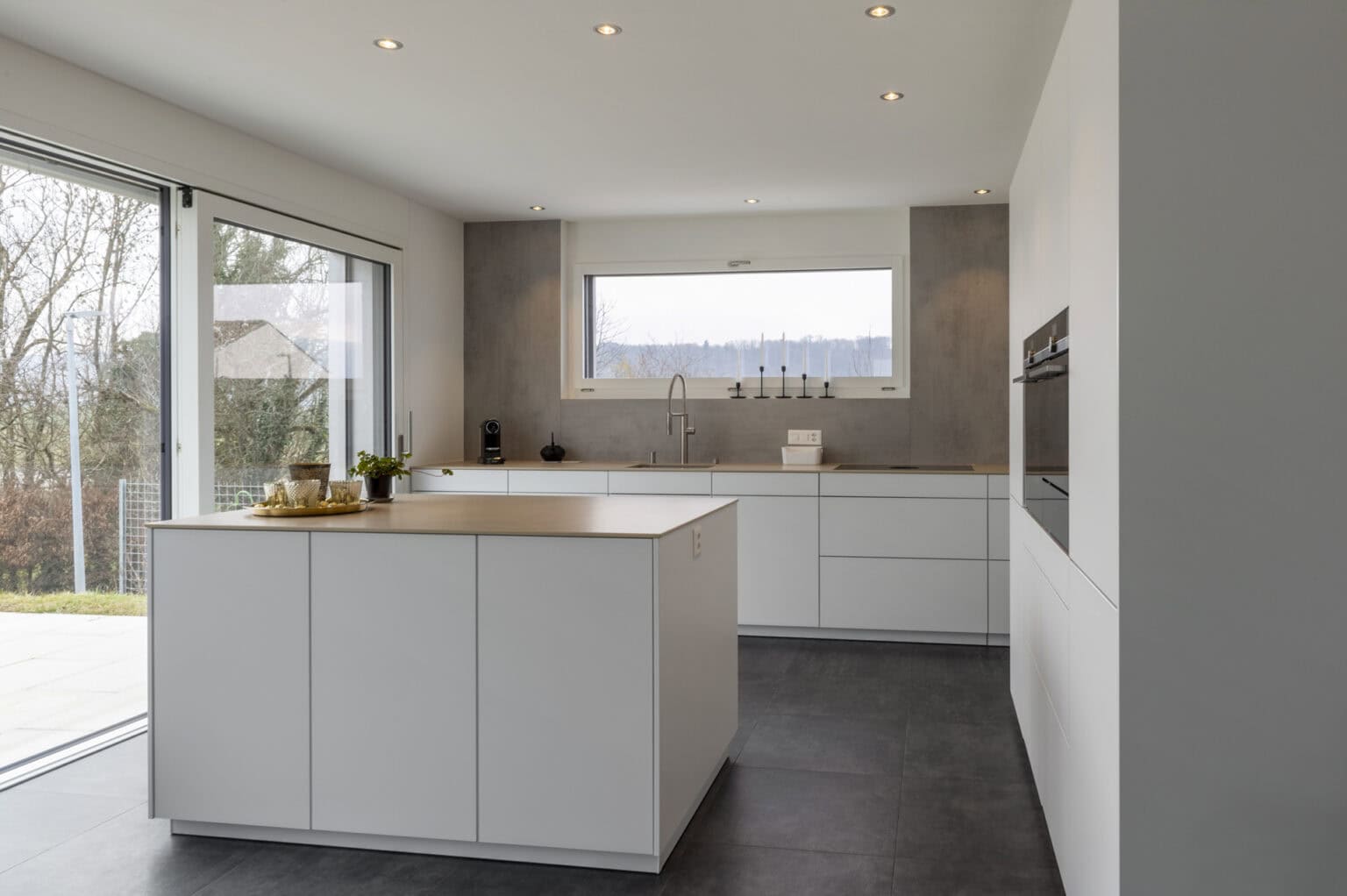 Weiße Küche mit Insel, viel Tageslicht und moderner Ausstattung für stilvolles Kochen.