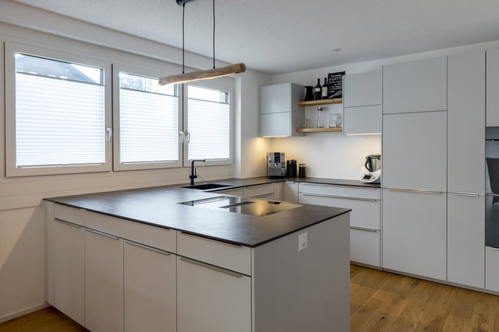 Moderne weiße Küche mit Insel und viel Stauraum, helle Fenster.