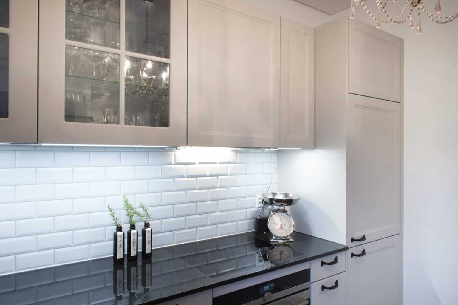 Moderne weiße Küche mit schwarzen Arbeitsplatten, weißen Fliesenspiegel und eleganten Schränken.