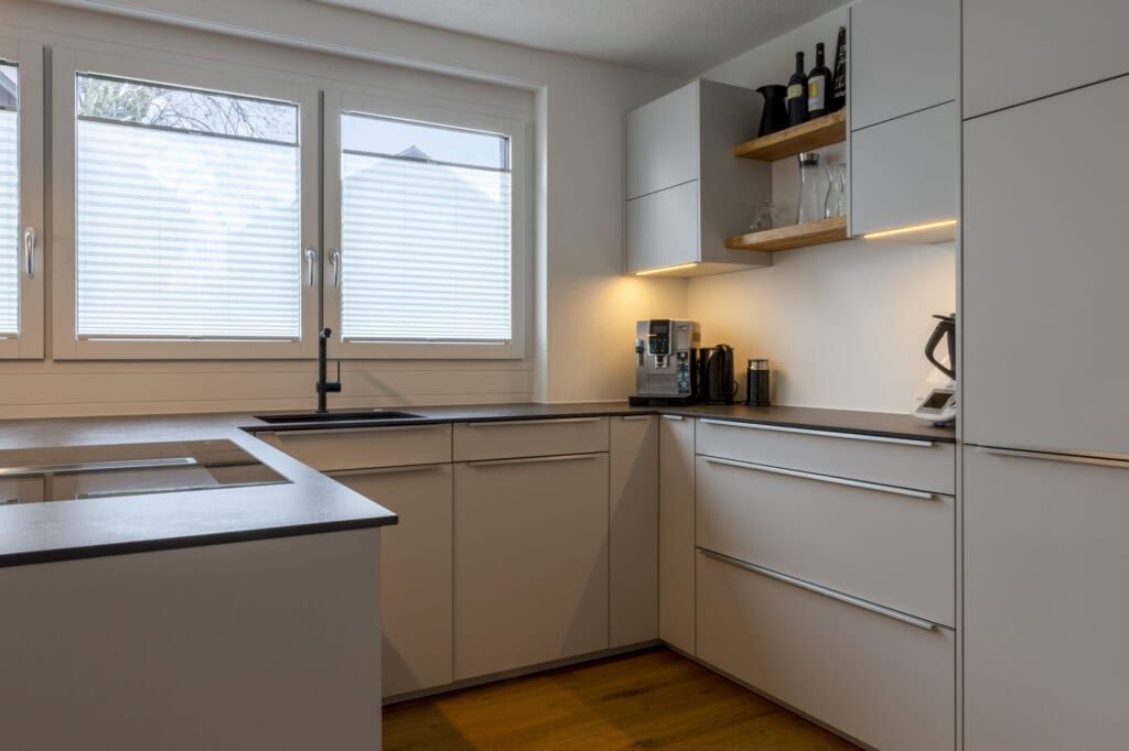 Moderne Küche mit weißen Schränken, Fenster und Küchenutensilien.