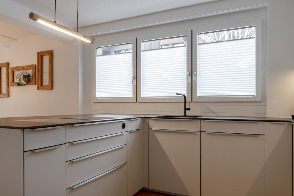 Moderne Küche mit weißen Schränken, viel Tageslicht und minimalistischer Gestaltung.